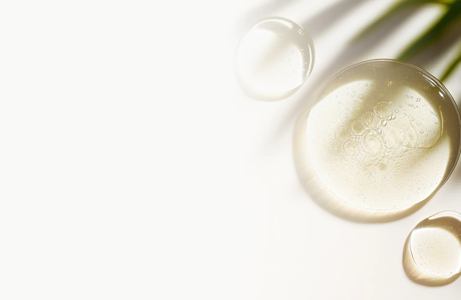 Clear glycerin drops on a white surface with soft shadows