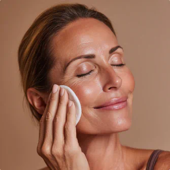 Smiling woman gently applying a cotton pad to her cheek with eyes closed