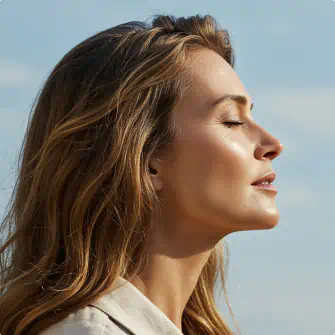 Peaceful woman with glowing skin facing the sun with eyes closed