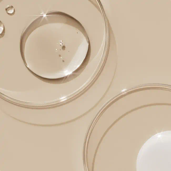 Clear skincare serum droplets in glass petri dishes on a beige background